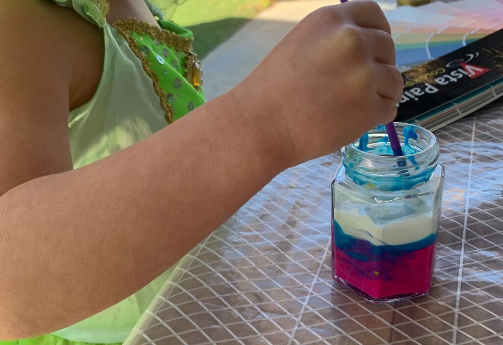 Photo of child mixing pink, blue, and white paint together with color wheel in background